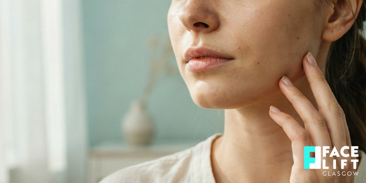 Photorealistic close-up of a woman’s lower face and jawline in soft daylight, her fingertips resting lightly along the jaw, conveying a natural focus on the areas facial tightening targets
